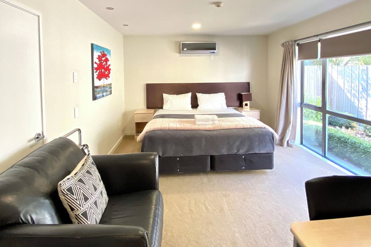 Une chambre d’hôtel moderne, dotée d’un grand lit, d’un canapé, d’une petite table et offrant une vue sur l’extérieur.