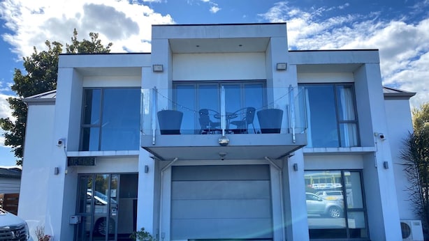 A modern two-story house with a garage, a balcony with outdoor furniture, and a clear sky. - Alpha Motel Christchurch (Christchurch)