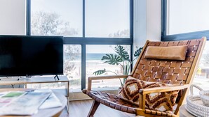 A room with a large window, a television, a wooden chair with a patterned cushion, and a round table with papers.