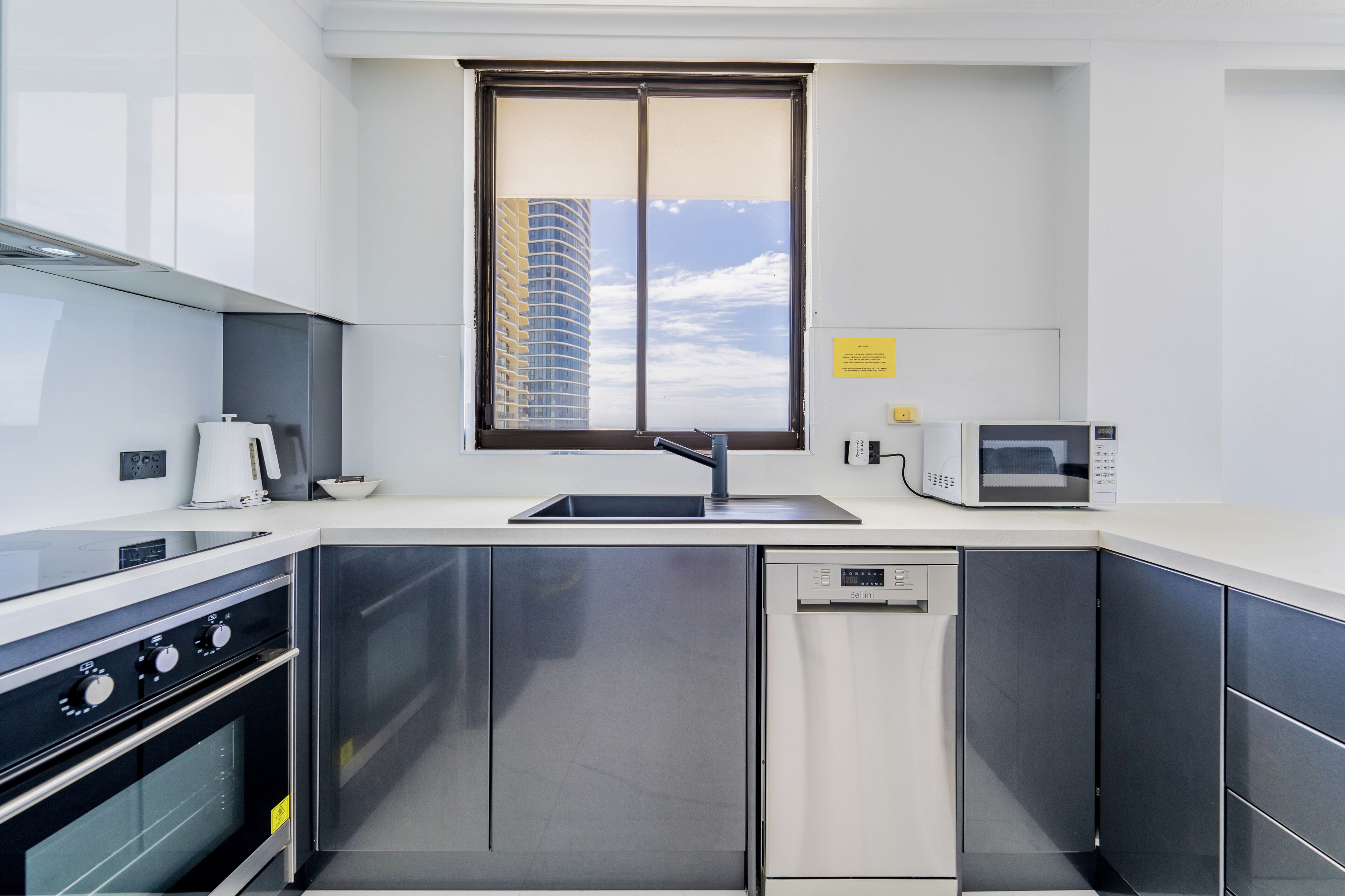 Eine moderne Küche mit Edelstahlgeräten, einem Backofen, einer Spülmaschine und einem Fenster mit Blick auf ein hohes Gebäude.
