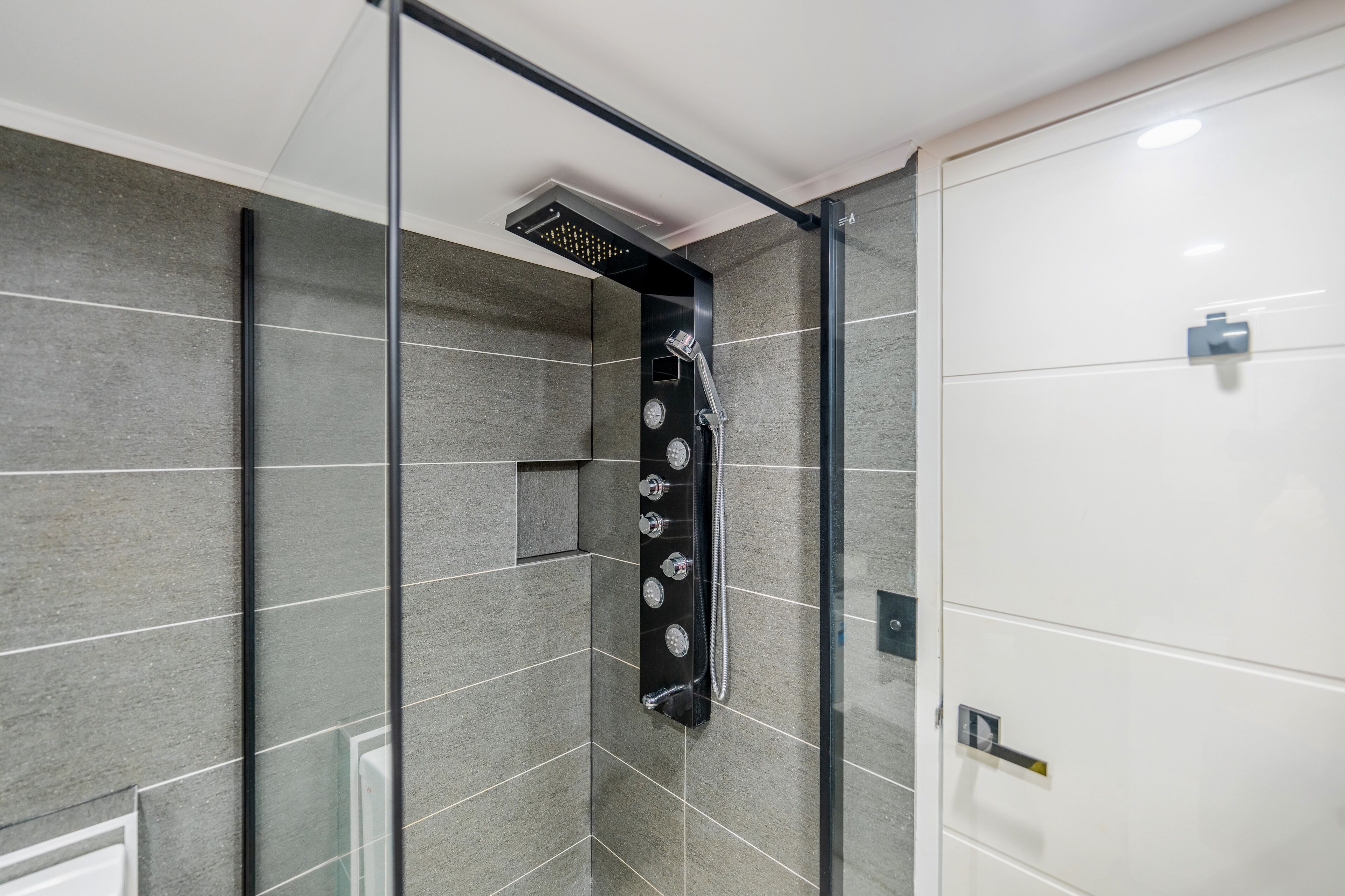 Eine moderne Dusche mit Glasabtrennung, grauen Fliesen und einer Bedienkonsole mit mehreren Drehreglern.