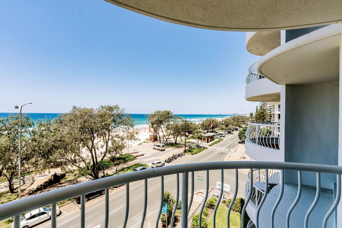 A balcony with a view of a coastal road, trees, and a clear blue sky.