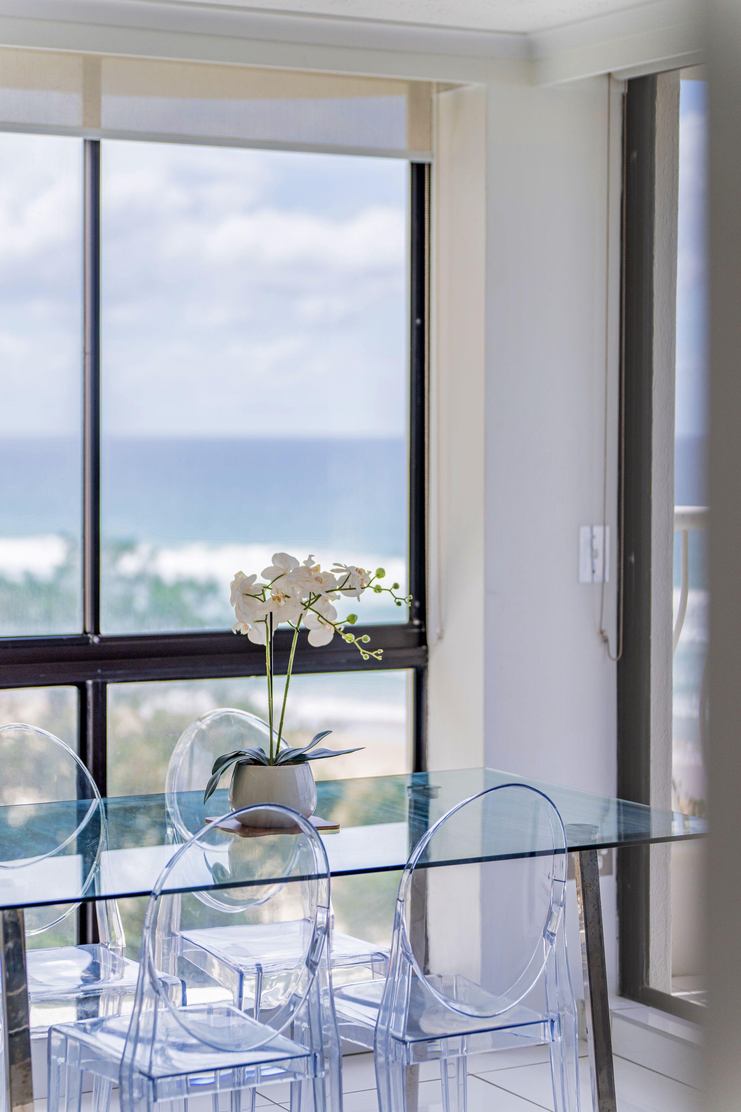 Une table à plateau en verre, des chaises transparentes et une plante en pot.