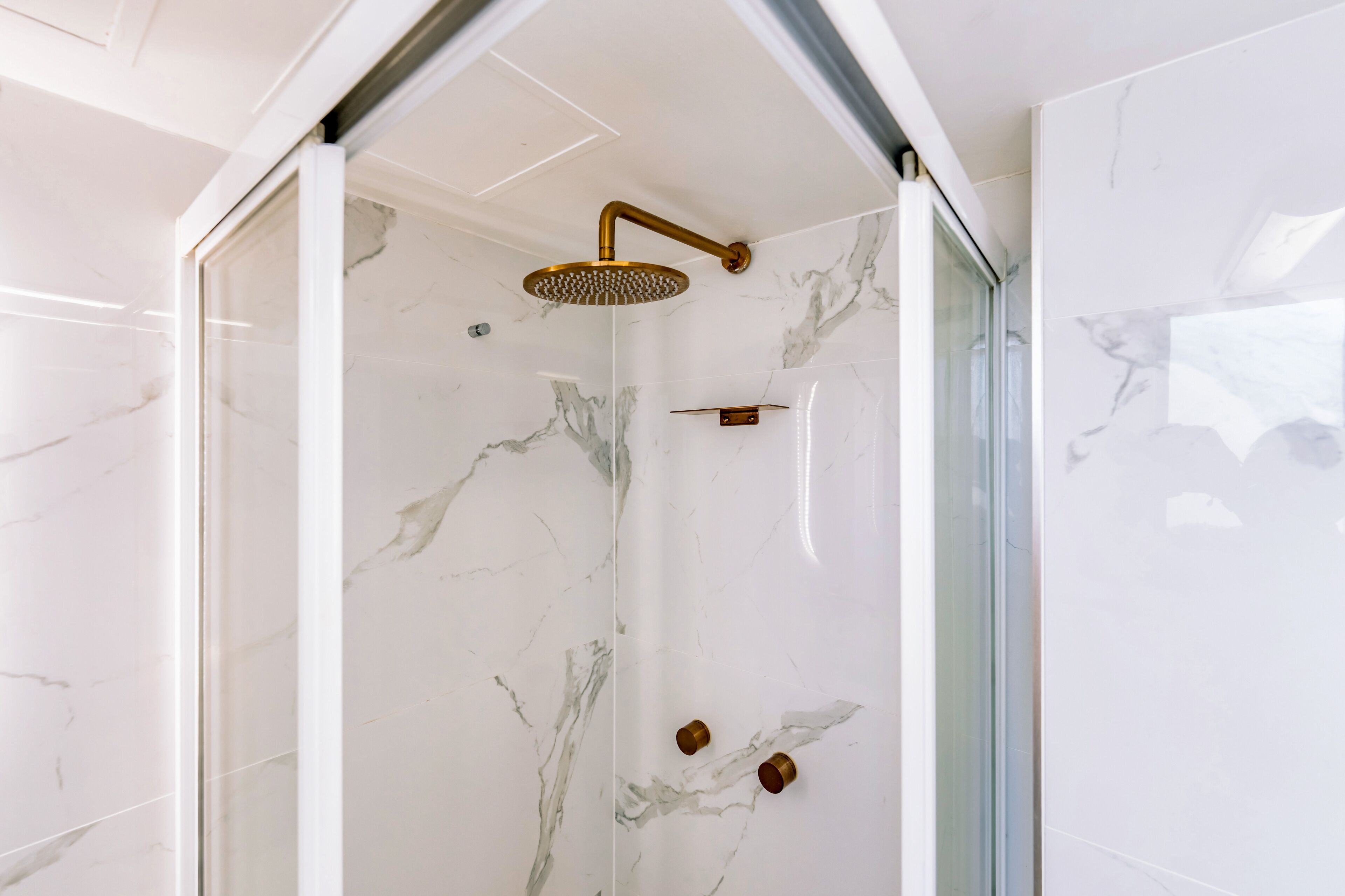 A modern shower with a glass enclosure and marble walls.