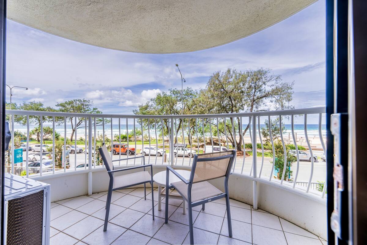 A balcony with a view of the beach and parked cars.
