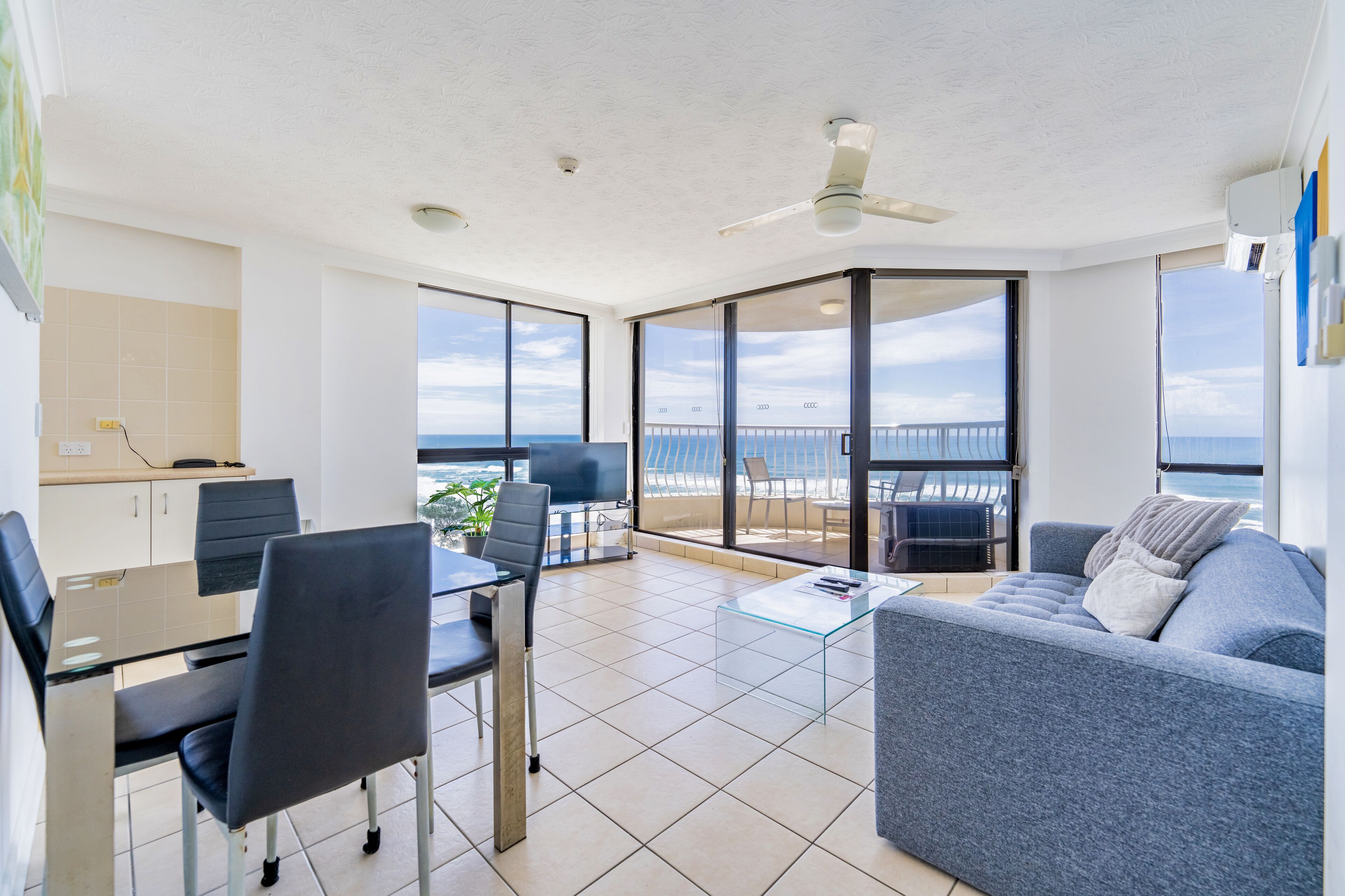 Una sala de estar moderna con balcón y vistas al mar, que incluye un sofá, sillas, una mesa de centro y un comedor.