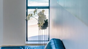 A room with a large window overlooking a beach, a blue sofa, and a wall-mounted painting.