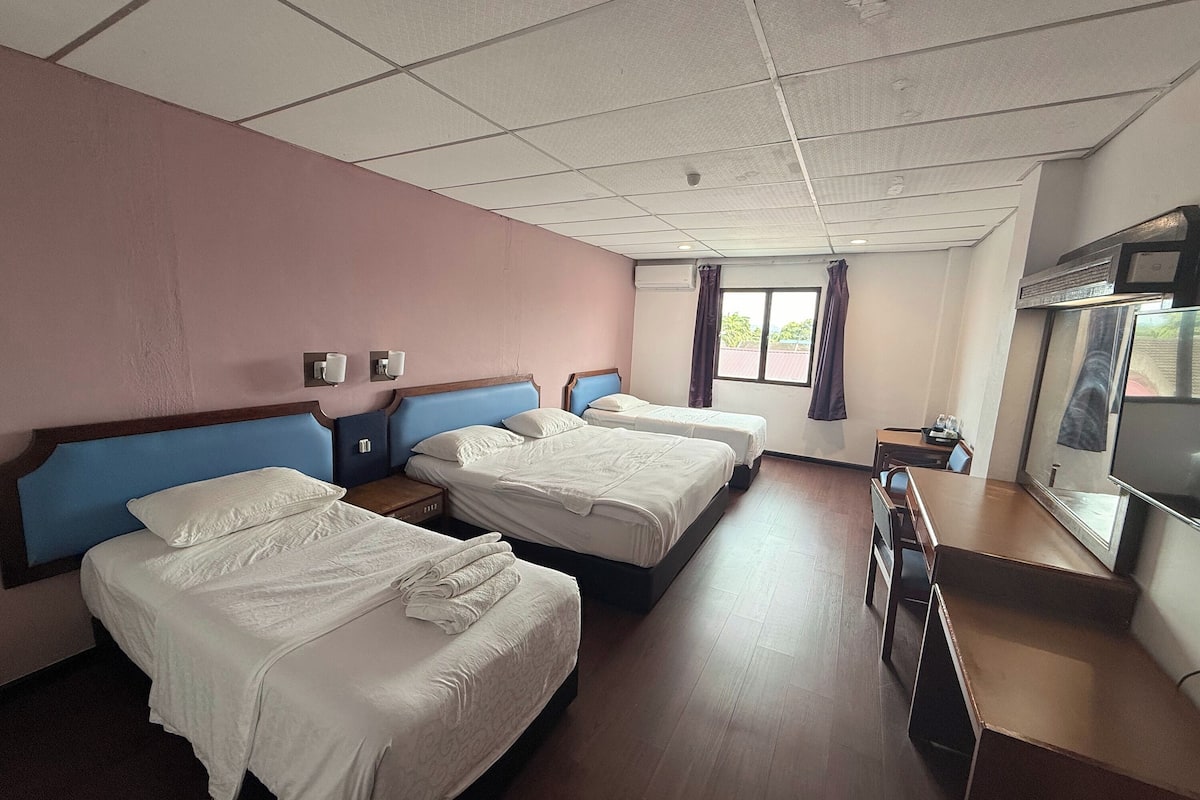 A hotel room with two beds, a TV, a window with curtains, and a wooden floor.