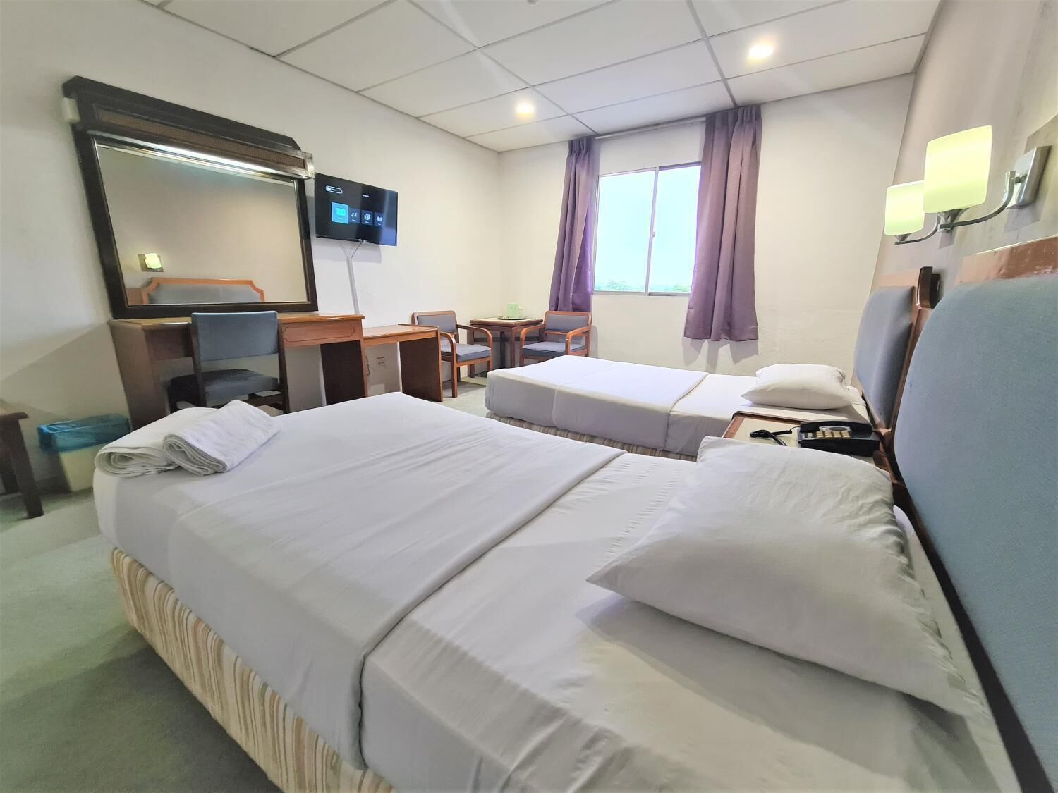 A hotel room with two beds, a desk, a chair, a TV, and a window with curtains.
