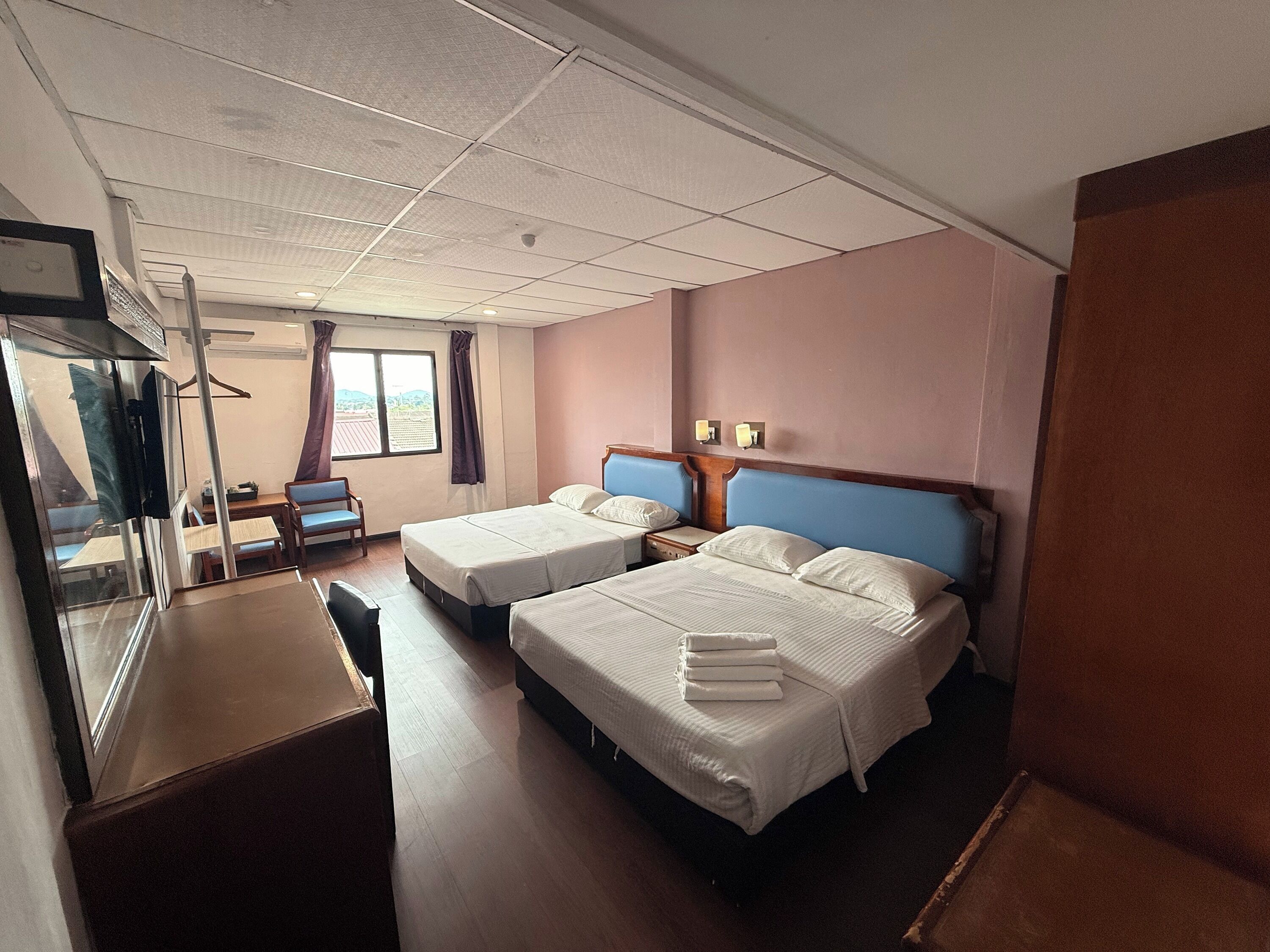 A hotel room with two beds, a desk, a chair, a TV, and a window with curtains.