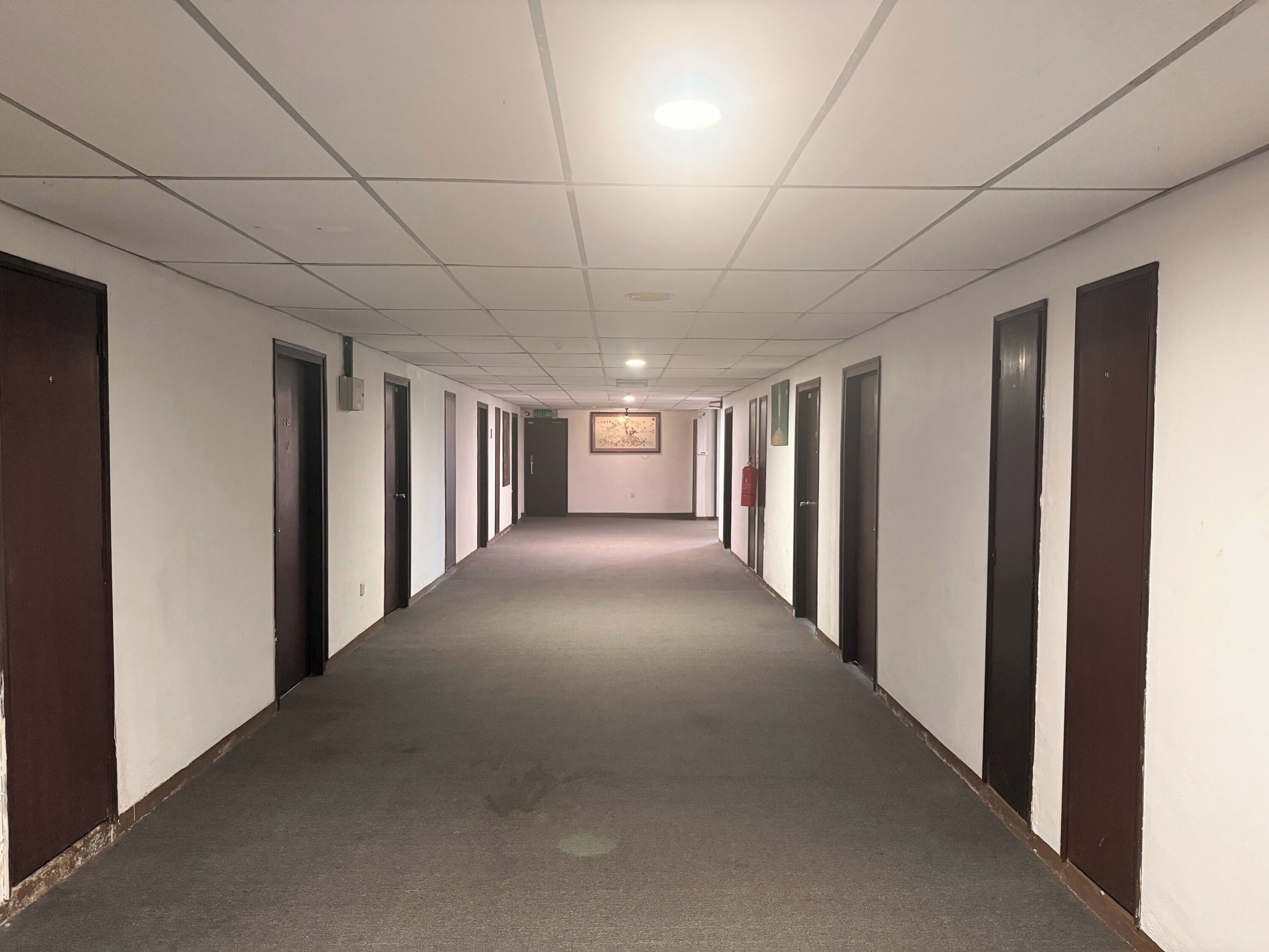 Ein langer, schmaler Korridor mit Türen an beiden Seiten, Teppichboden und einer Decke mit eingelassenen Leuchten.