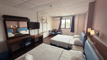 A hotel room with two beds, a desk with a chair, a TV, a desk lamp, and a window with curtains.