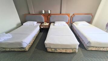 Habitación de hotel con tres camas individuales, una mesita de noche de madera con un teléfono y una alfombra estampada.