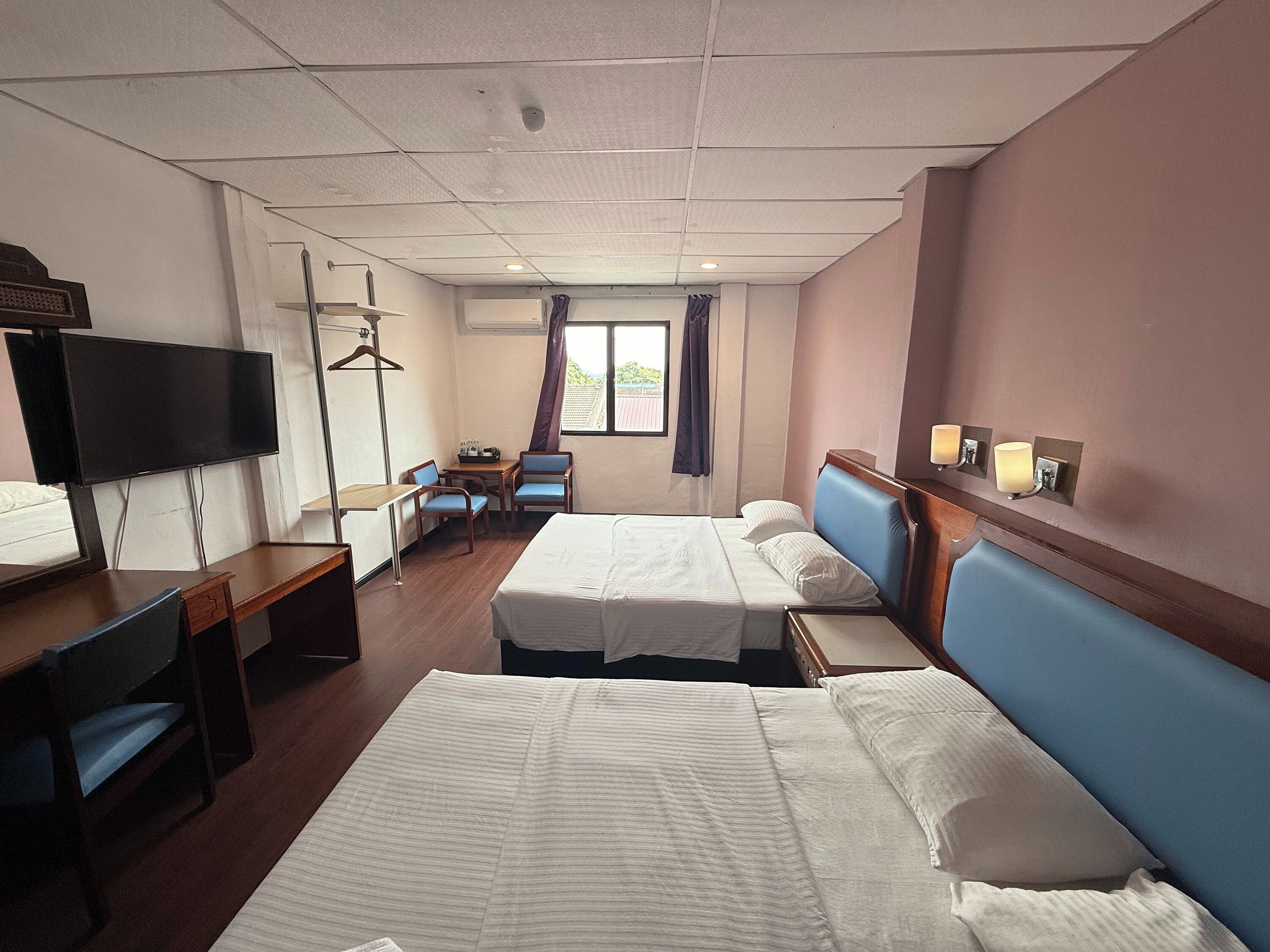 A hotel room with two beds, a desk, a TV, and a window with curtains.