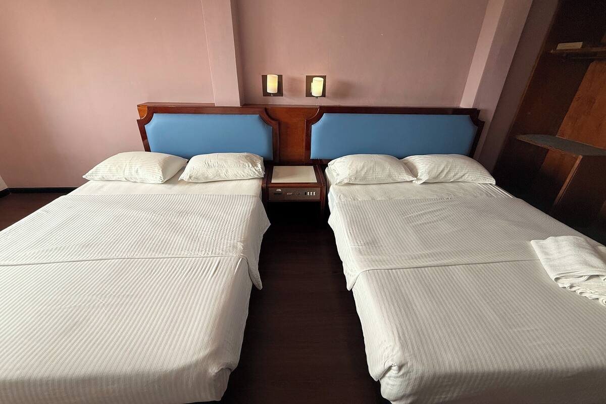 A hotel room with two single beds, a wooden headboard, a nightstand, and a wall-mounted lamp.
