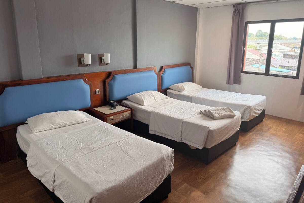 A hotel room with two beds, a wooden headboard, a nightstand, and a window with a view of buildings.
