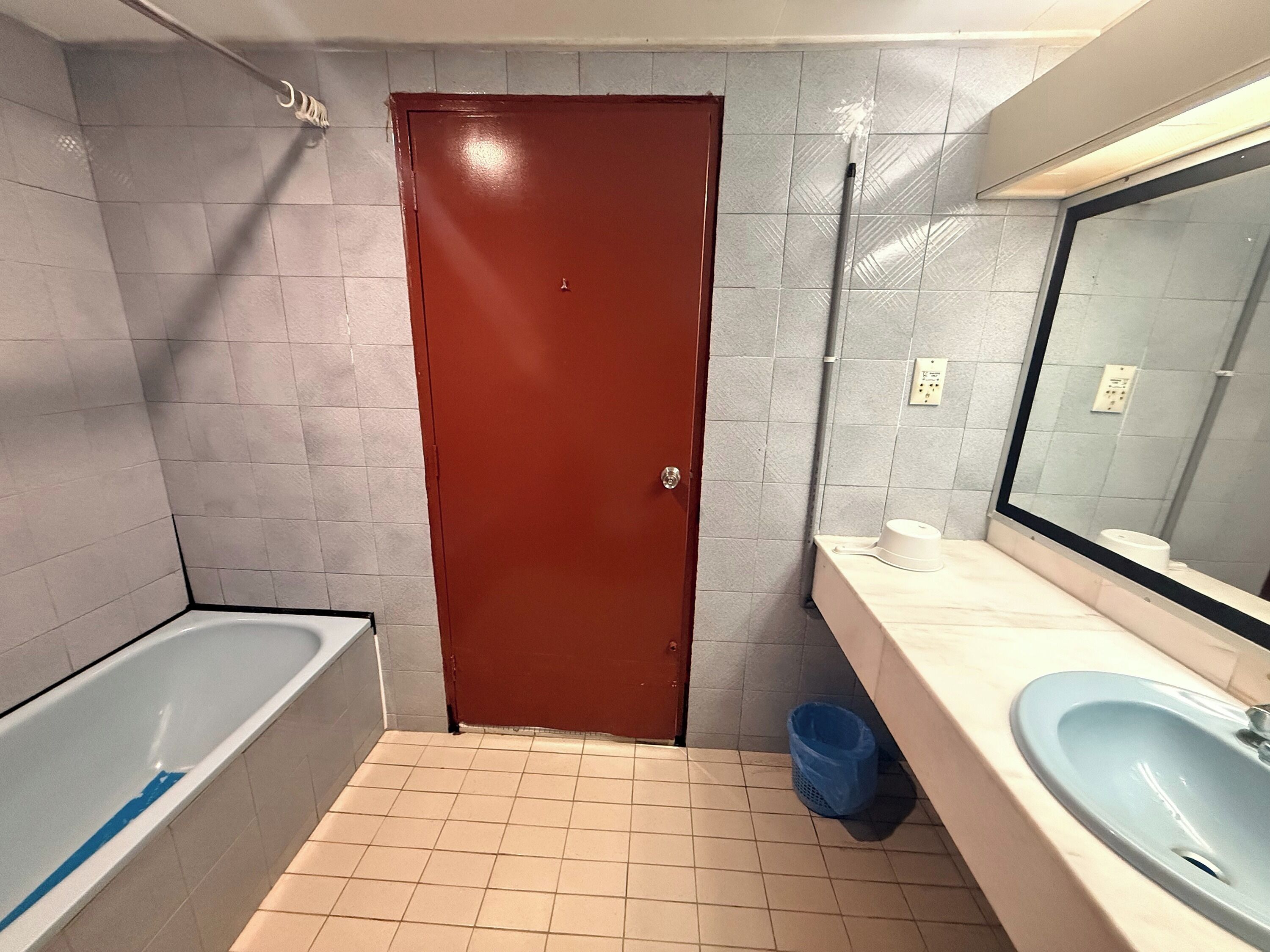 A bathroom with a bathtub, a sink, a mirror, and a door.