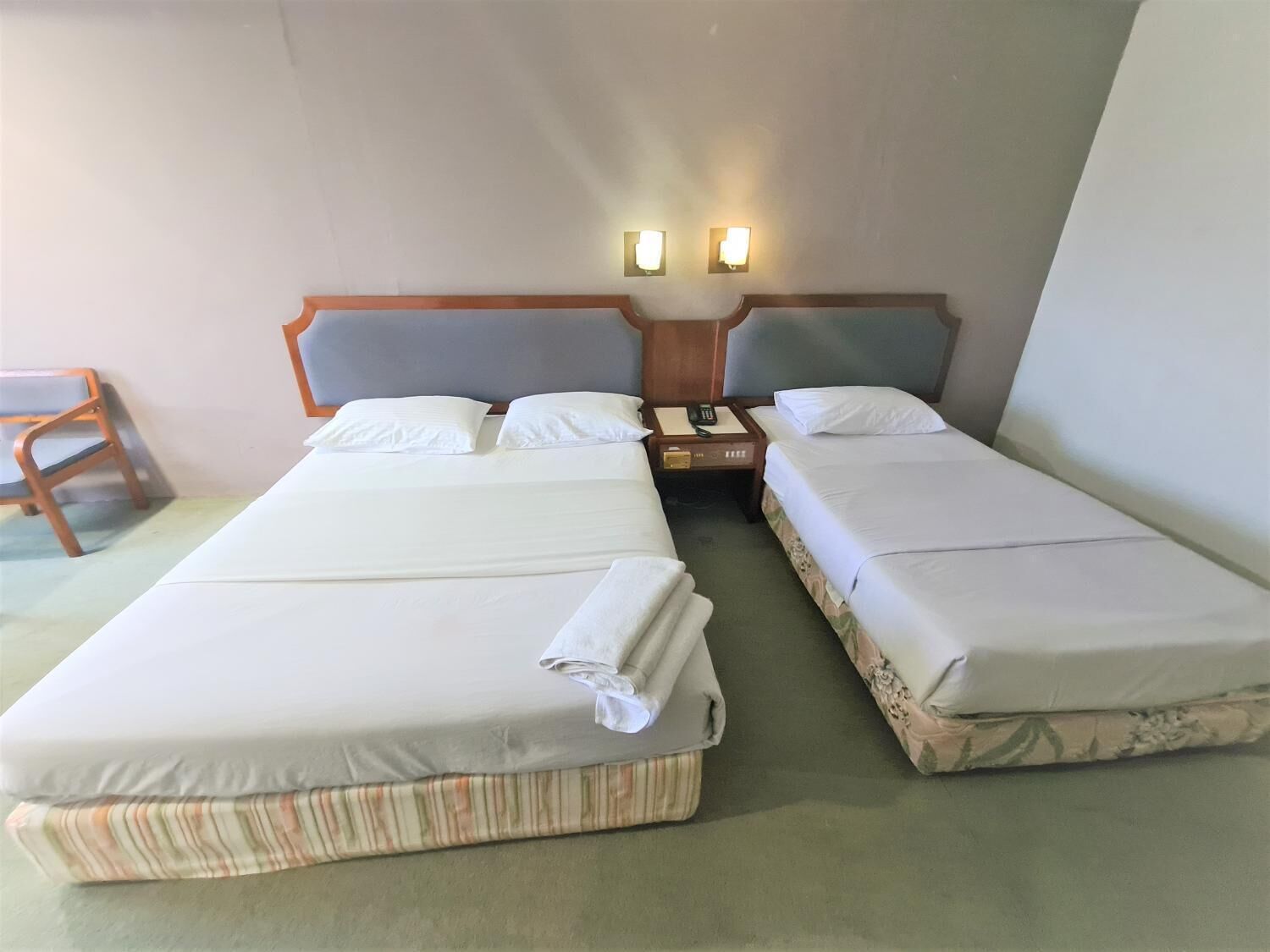 A hotel room with two beds, a nightstand, and a chair.