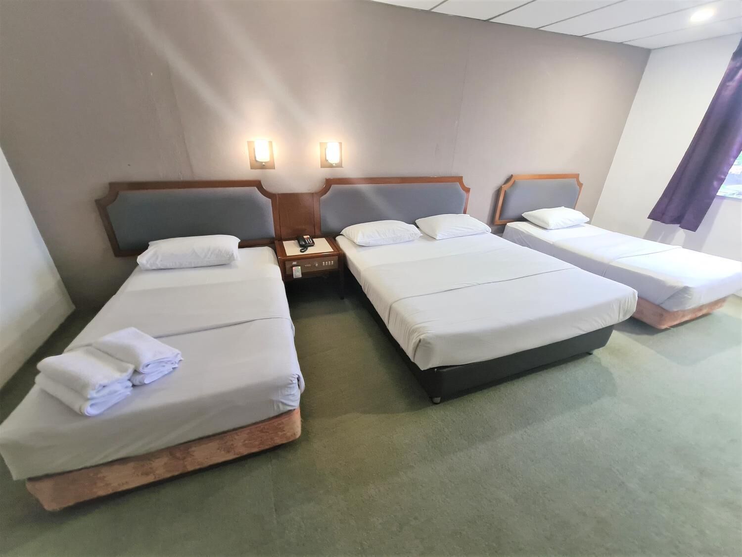 Una habitación de hotel con tres camas individuales, una mesita de noche con teléfono y dos lámparas de pared.