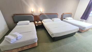 Una habitación de hotel con tres camas individuales, una mesita de noche con teléfono y dos lámparas de pared.