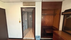 A hotel room with a wooden bench, a small trash bin, and a door leading to a bathroom.