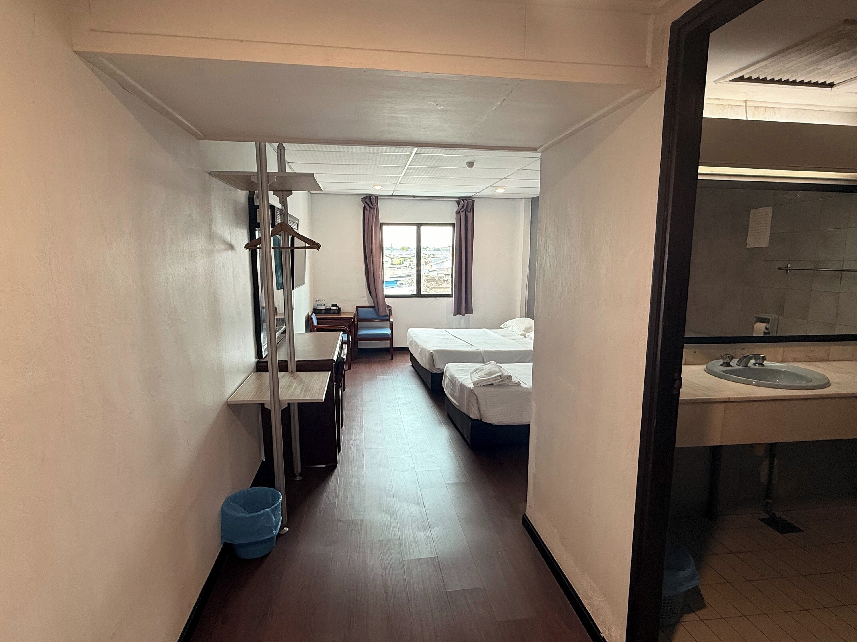 Une chambre d’hôtel équipée d’un bureau, de deux lits, d’une salle de bain avec un lavabo et d’une fenêtre avec des rideaux.