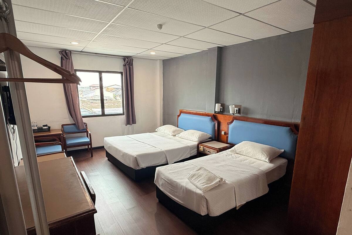 A hotel room with two beds, a desk, a chair, and a window with curtains.