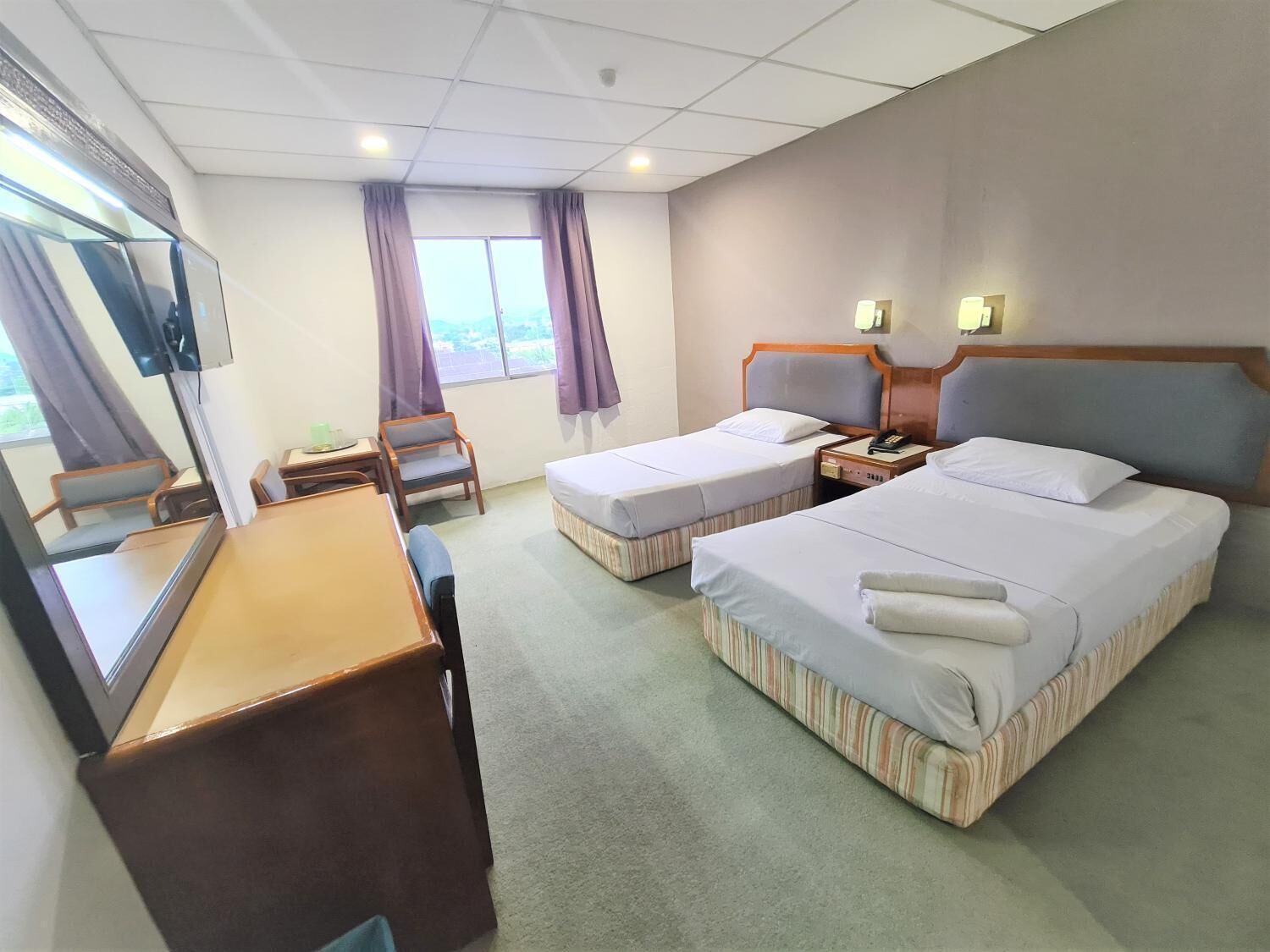 A hotel room with two single beds, a desk, a chair, a TV, and a window with curtains.