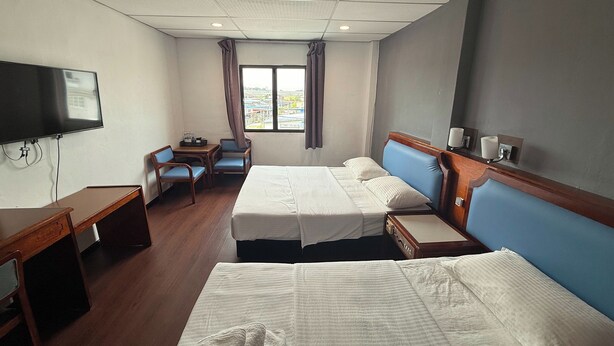 A hotel room with two beds, a desk, a TV, and a window with curtains.