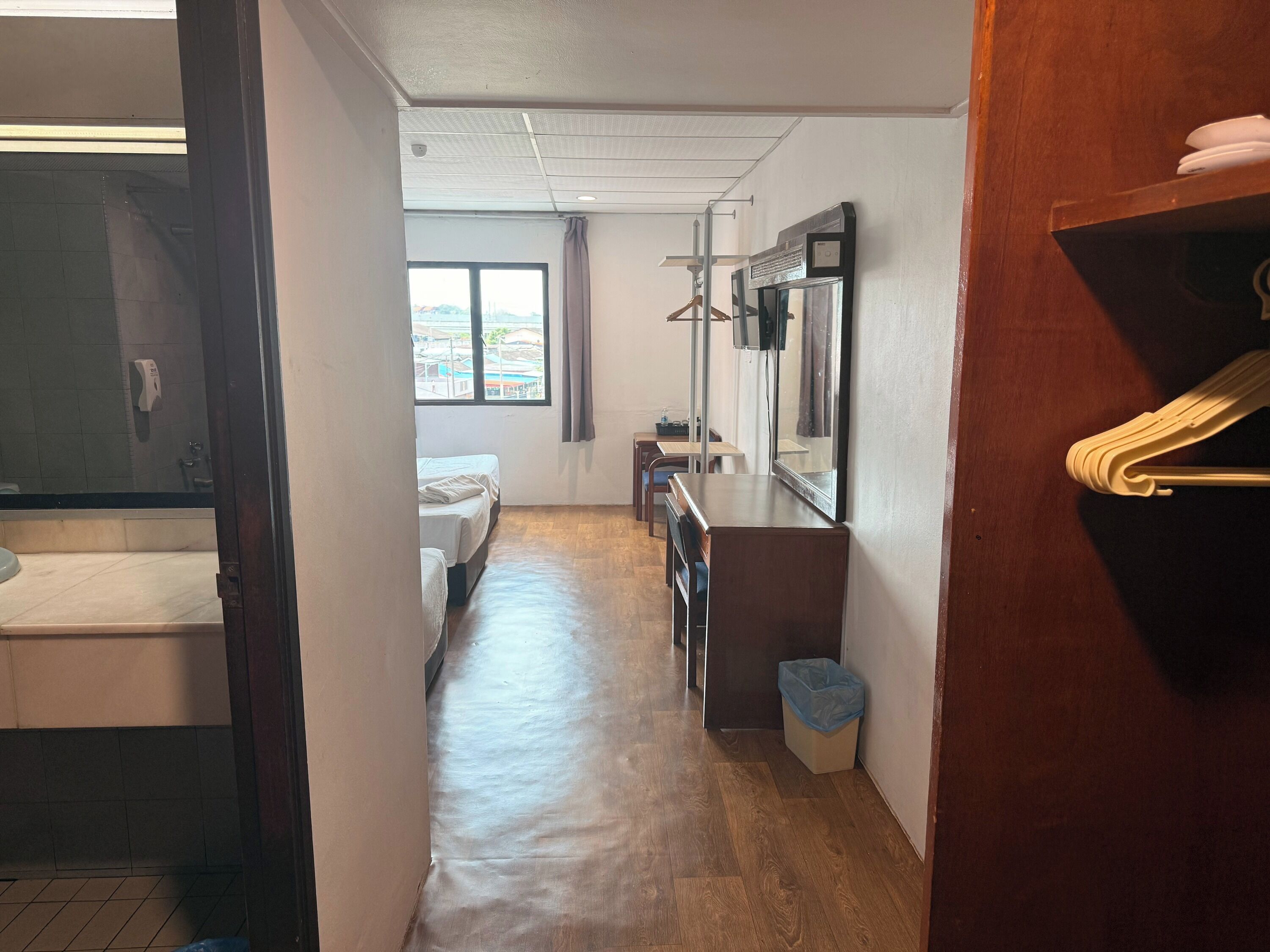 Habitación de hotel con piso de madera, cama, escritorio, espejo y ventana con vista a edificios.