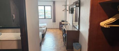 Habitación de hotel con piso de madera, cama, escritorio, espejo y ventana con vista a edificios.