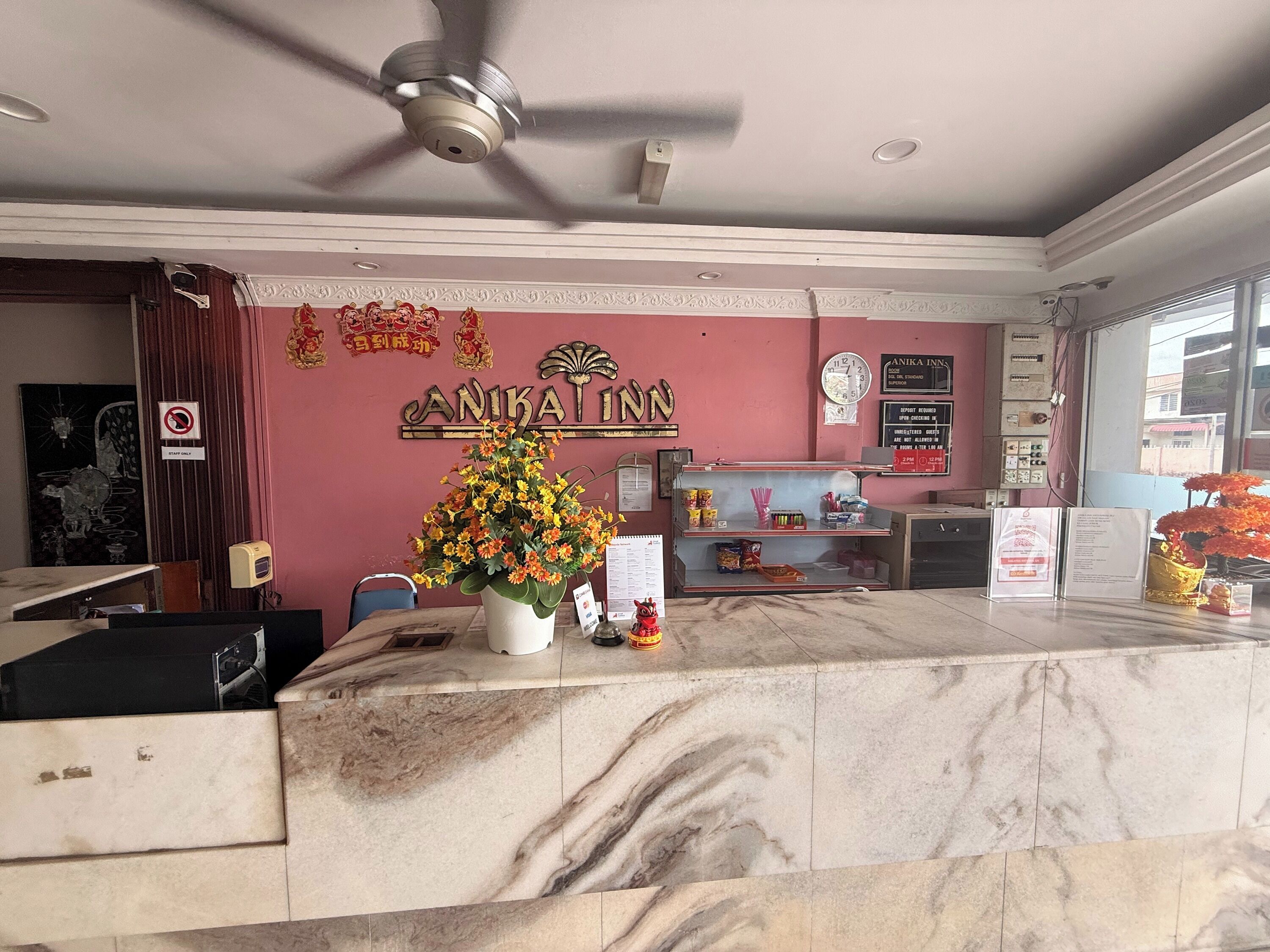 A reception area with a marble counter, a ceiling fan, a clock, and a wall with a sign that reads "ANKAT INN".