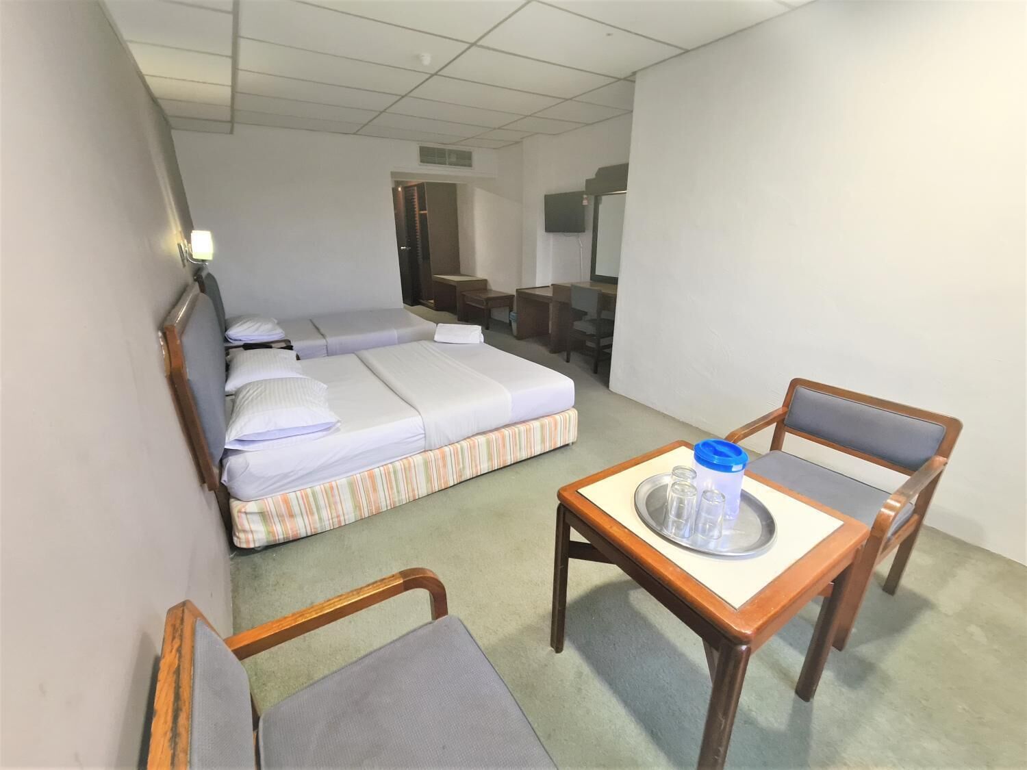 Hotellihuone, jossa on sänky, pieni pöytä tarjottimella, kaksi tuolia ja televisio.