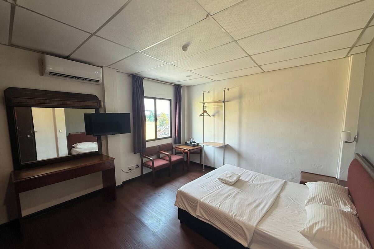 A hotel room with a bed, a desk, a chair, a TV, and a window with curtains.