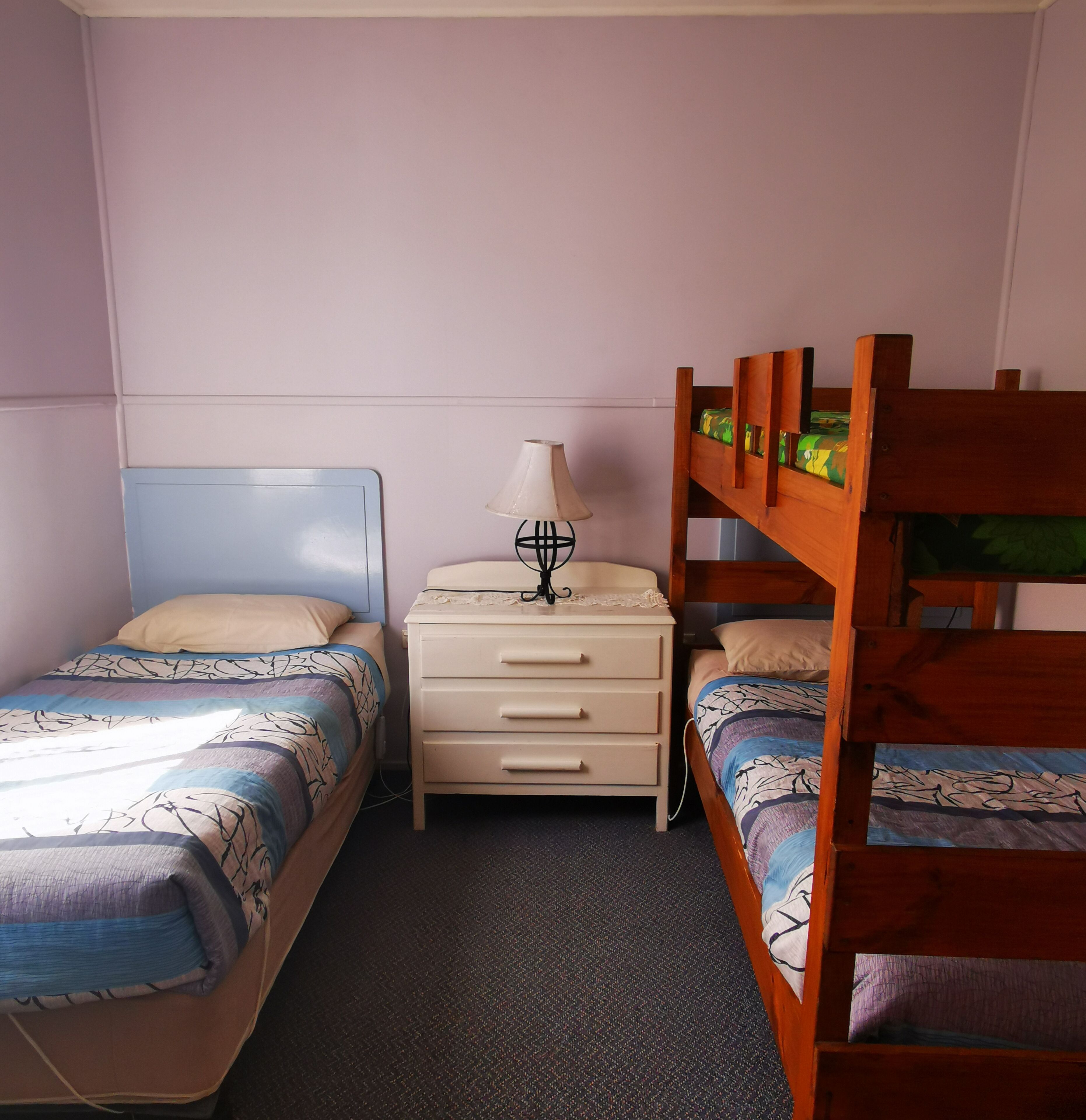 A bedroom with two single beds, a nightstand with a lamp, and a dresser.