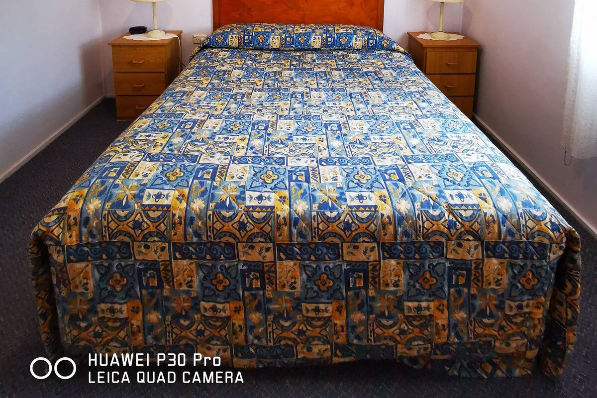 A hotel room with a bed, two bedside tables, a nightstand, a wall-mounted flag, and a window with curtains.