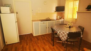 A compact kitchen with a refrigerator, microwave, and sink. There is a dining table with chairs and a small window with curtains. - Anchorage Holiday Units (Lakes Entrance)