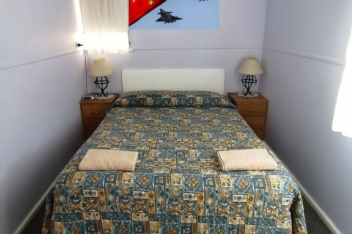 A bedroom with a bed, two bedside tables, a wall-mounted flag, and a window with curtains.