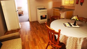 A compact kitchen with a gas stove, oven, and sink. A dining table with chairs is in the foreground. - Anchorage Holiday Units (Lakes Entrance)
