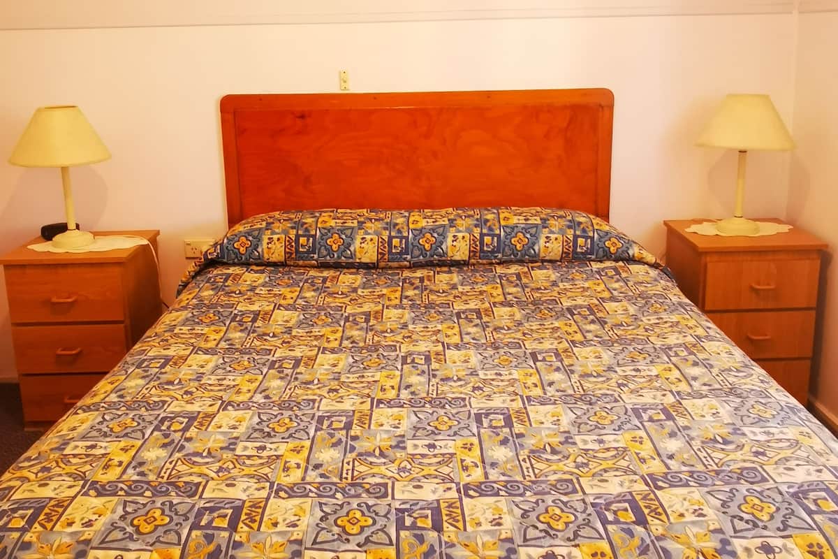 A bed with a patterned bedspread, two bedside tables with lamps, and a wooden headboard.