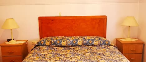 A bed with a patterned bedspread, two bedside tables with lamps, and a wooden headboard.