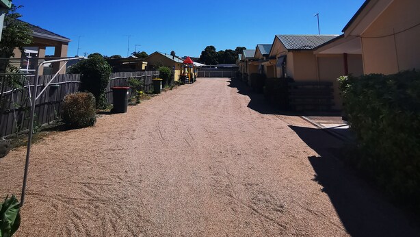 A residential area with a gravel driveway leading to a house with a red roof. - Anchorage Holiday Units (Lakes Entrance)