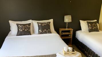A hotel room with two beds, a nightstand, a lamp, and a window with a view of trees.