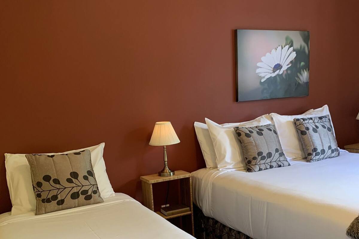 Ein Hotelzimmer mit zwei Betten, einem Nachttisch mit Lampe und einem an der Wand hängenden Blumenbild.