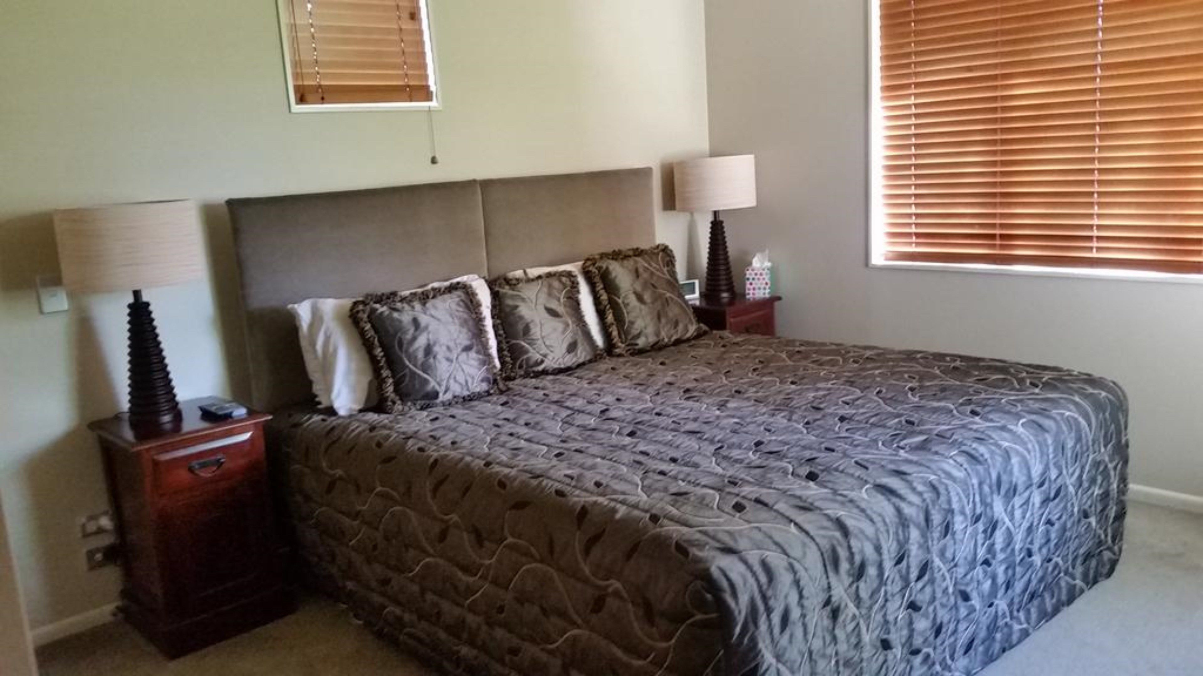 A neatly made bed with a patterned bedspread, two bedside tables with lamps, and a window with blinds.