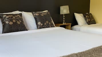 Een hotelkamer met twee bedden, donkere muren, een raam en een nachtkastje met een lamp.