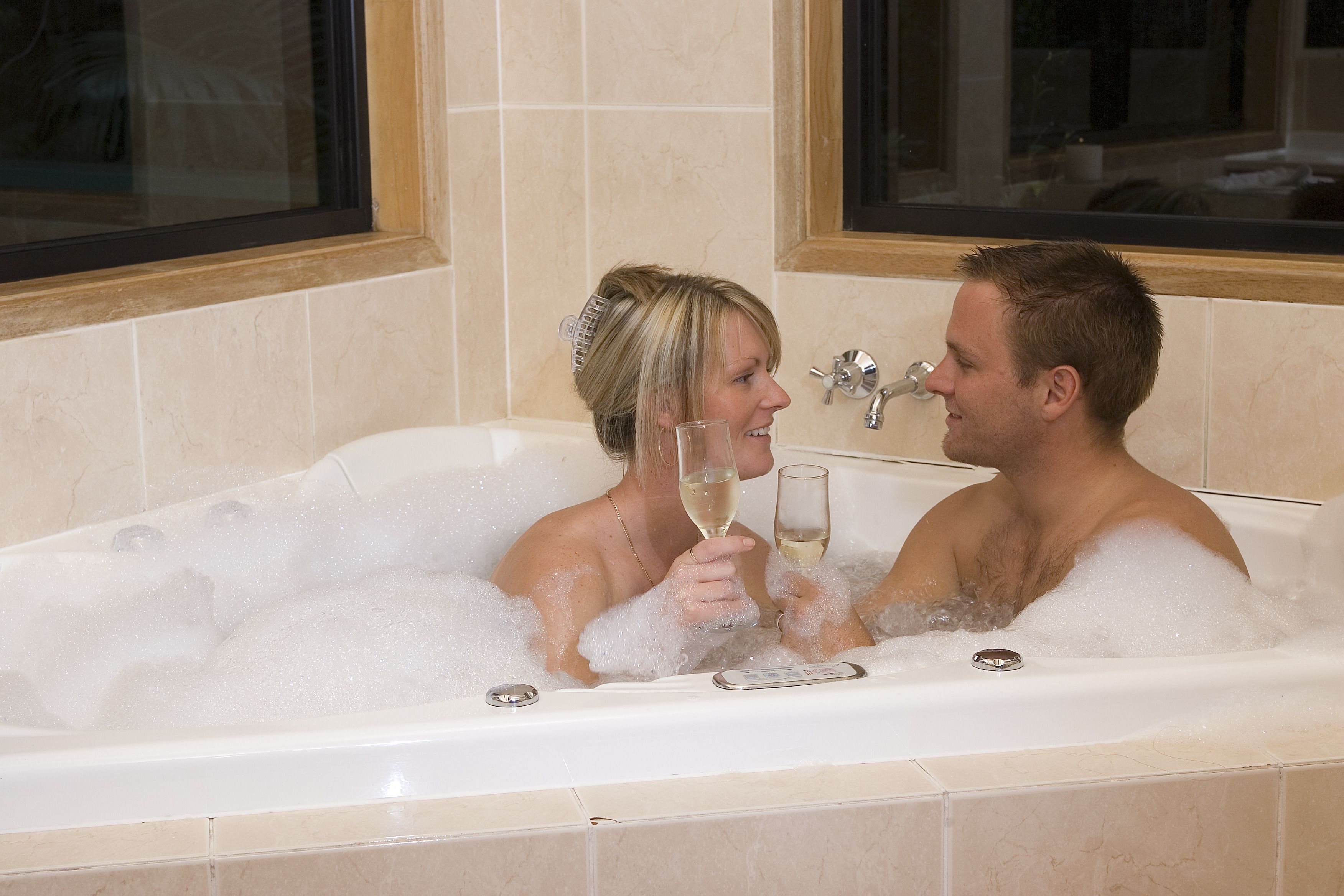 A couple in a bathtub filled with bubbles, holding glasses of champagne.