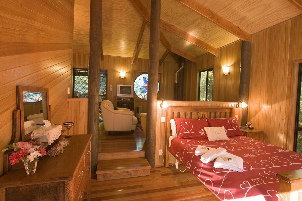 Un interior de madera con una cama, un aparador, un espejo y una ventana con diseño de vitral.