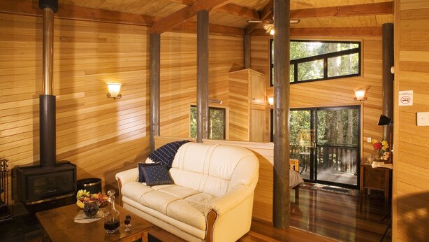 L’intérieur chaleureux d’un chalet avec un canapé, une table avec des boissons, une cheminée et de grandes fenêtres.