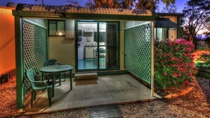 A small, enclosed patio area with a table and chairs, a door leading to a kitchen, and a green fence. - Goondiwindi Holiday Park (Goondiwindi)